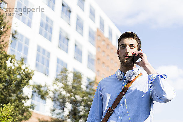 Junger Mann benutzt Smartphone  Kopfhörer um den Hals in der Stadt