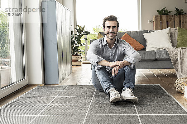 Selbstbewusster junger Mann sitzt auf dem Boden seines Wohnzimmers