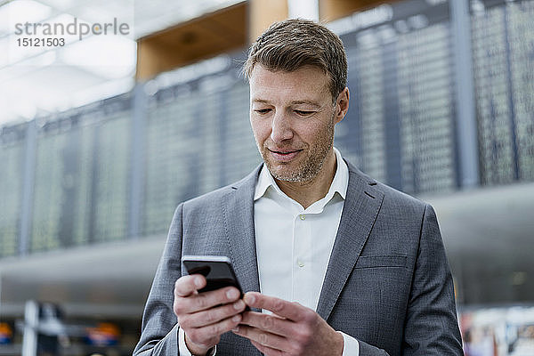 Porträt eines Geschäftsmannes  der auf dem Flughafen ein Mobiltelefon benutzt