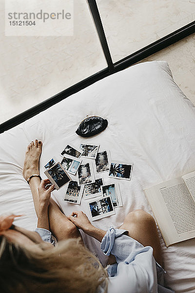 Junge Frau im Bett mit Buch und Polaroidbildern