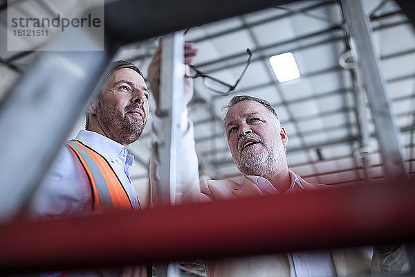 Geschäftsmann und Mann in reflektierender Weste im Gespräch in der Industriehalle