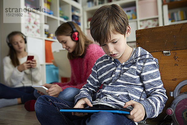 Geschwister  die zu Hause mit ihren digitalen Tabletts spielen und auf dem Boden sitzen