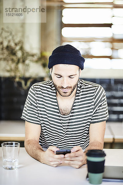 Junger Mann trägt eine Mütze und benutzt ein Mobiltelefon
