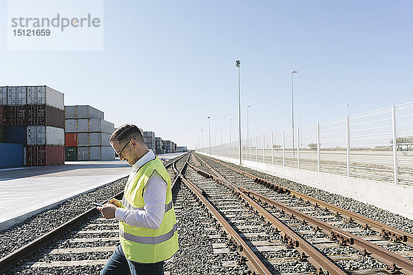 Mann auf Eisenbahnschienen vor Frachtcontainern mit Handy