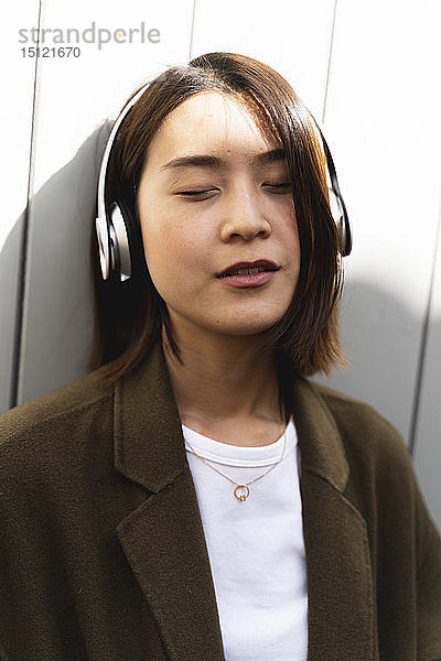 Entspannte junge Frau mit geschlossenen Augen  die mit Kopfhörern Musik hört