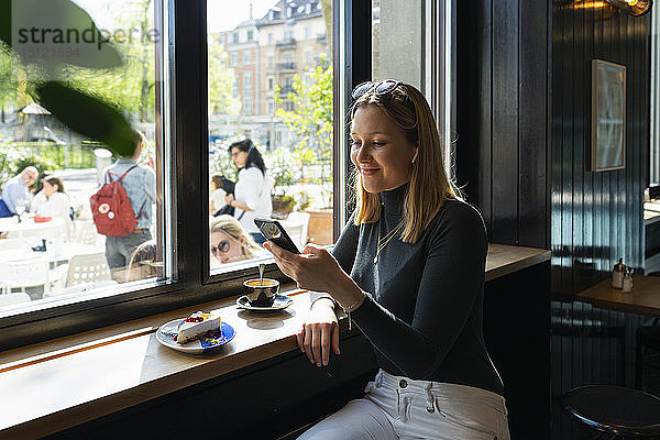 Lächelnde junge Frau in einem Café  die auf ein Smartphone schaut