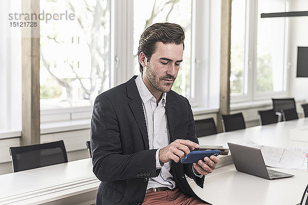 Junger Geschäftsmann sitzt im Sitzungssaal  benutzt ein Smartphone