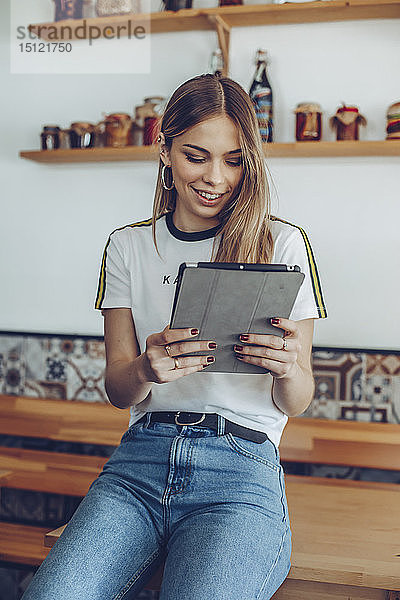 Porträt einer jungen Frau  die in einem Cafe mit einer Tablette lächelt