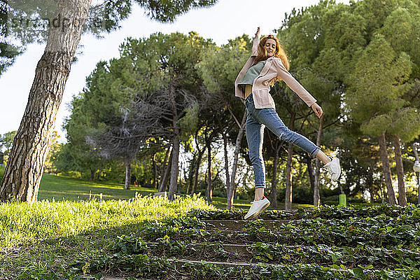 Junge rothaarige Frau springt in einem Park auf Treppen