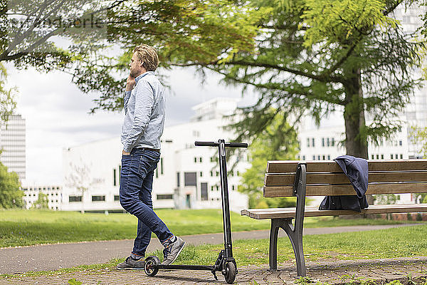 Geschäftsmann mit E-Scooter am Telefon im Stadtpark  Essen  Deutschland