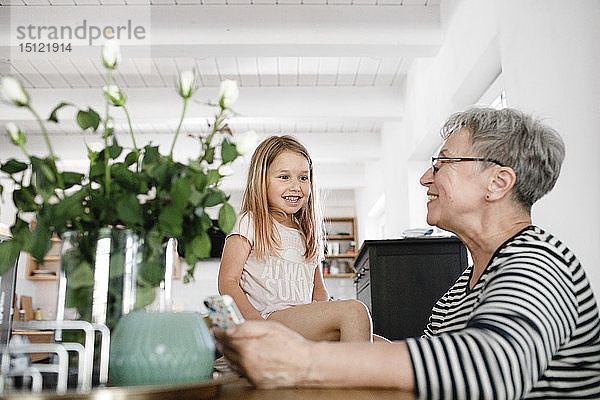 Glückliche Großmutter mit Handy und Enkelin zu Hause