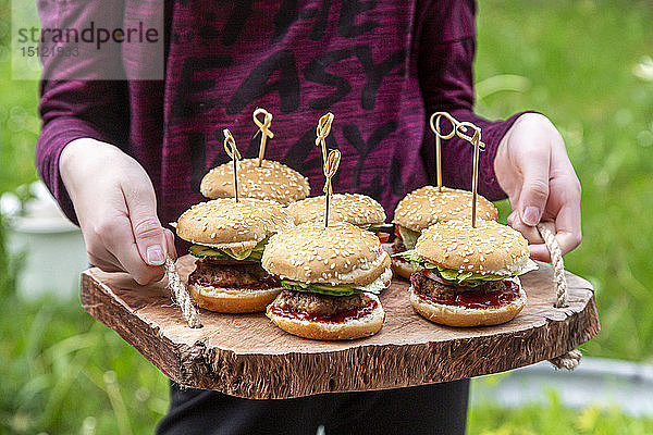 Mädchen hält Holztablett mit Mini-Burger