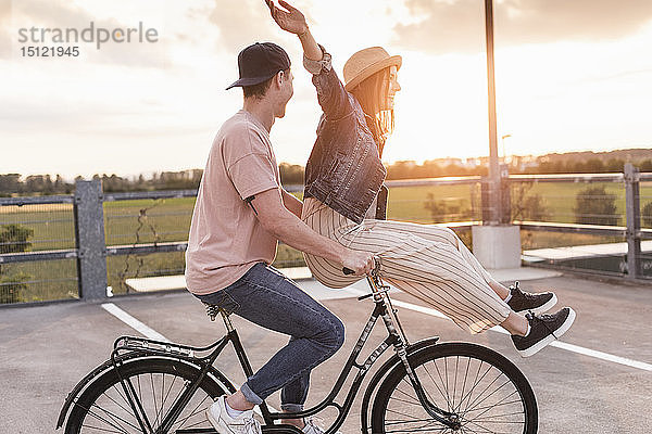 Glückliches junges Paar zusammen auf einem Fahrrad bei Sonnenuntergang auf dem Parkdeck