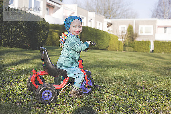 Porträt eines glücklichen kleinen Jungen mit Dreirad auf dem Rasen