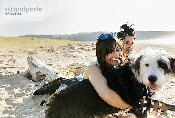 Zwei glückliche Frauen mit Hund am Strand