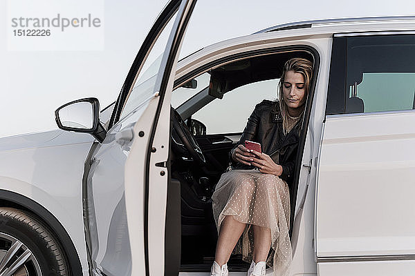 Blonde Frau mit Smartphone  die in einem weißen Auto sitzt