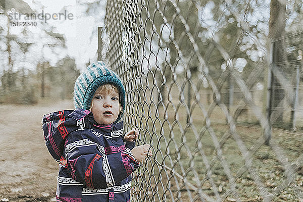 Bildnis eines Kleinkindes in warmer Kleidung an einem Zaun im Wald