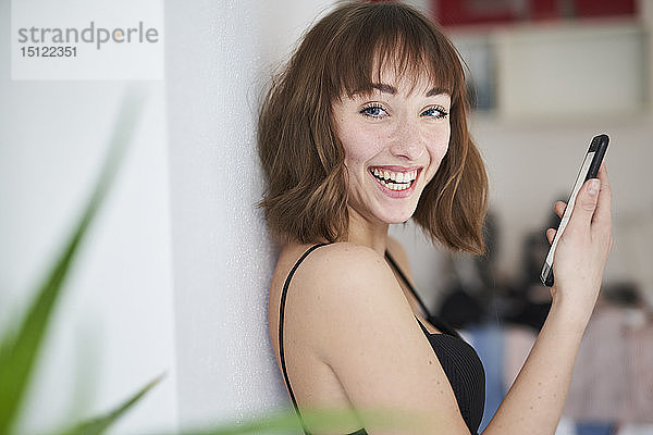 Porträt einer lachenden jungen Frau mit Smartphone zu Hause