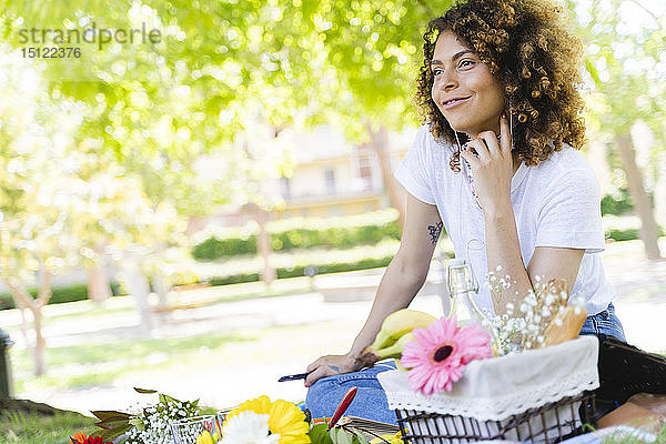 Entspannte Frau mit Handy und Kopfhörern beim Picknick im Park