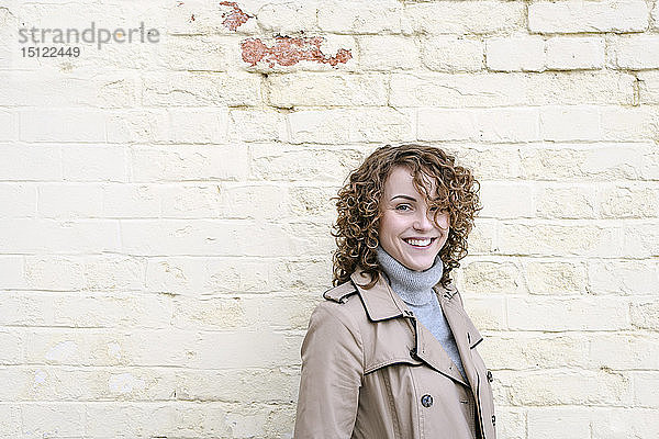 Porträt einer glücklichen Frau mit lockigem Haar vor einer Ziegelmauer