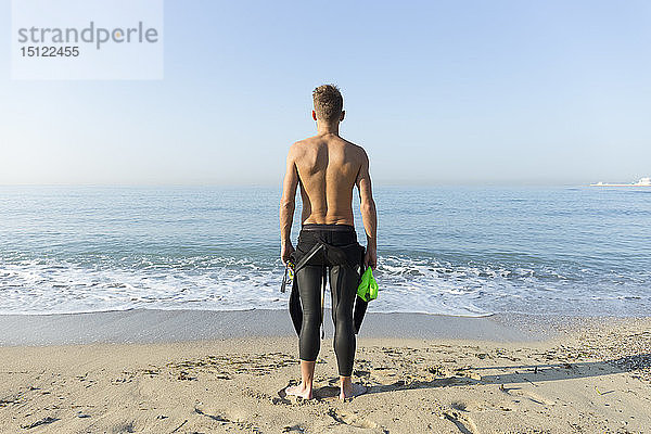 Rückansicht eines jungen Athleten am Strand  der sich auf das Schwimmen vorbereitet
