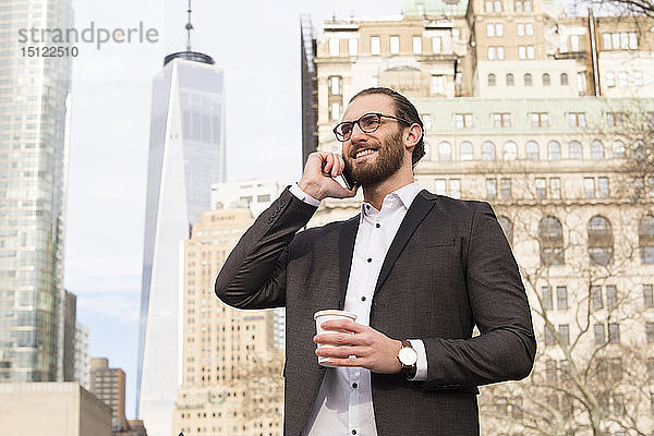 Lächelnder junger Geschäftsmann mit Kaffee zum Telefonieren  New York City  USA