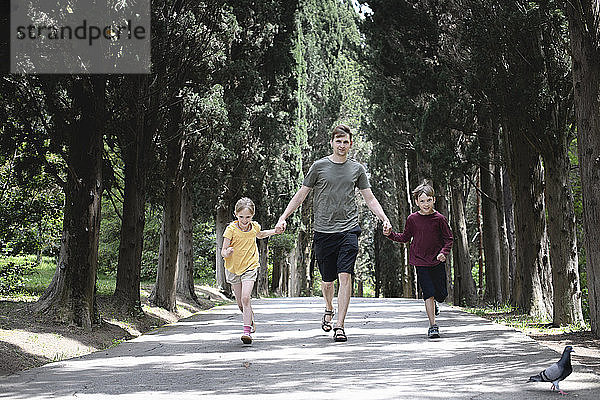 Vater mit zwei Kindern läuft auf einer Baumstraße