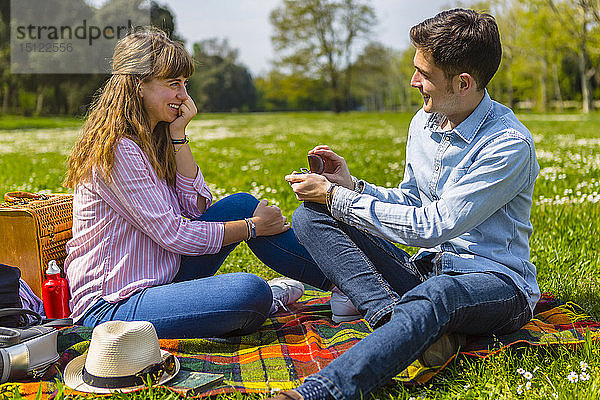 Junger Mann macht seiner Freundin in einem Park einen Heiratsantrag