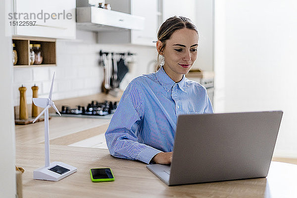 Frau arbeitet zu Hause am Laptop mit einem Windturbinenmodell auf der Küchentheke