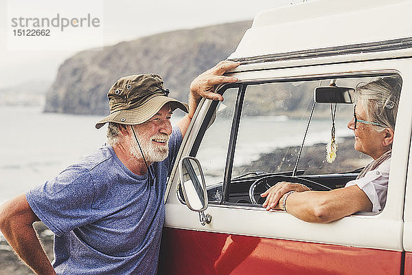 Älteres Ehepaar reist in einem Oldtimer-Van  macht eine Pause am Meer  unterhält