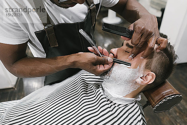 Mann lässt sich beim Friseur den Bart mit einem Rasiermesser rasieren
