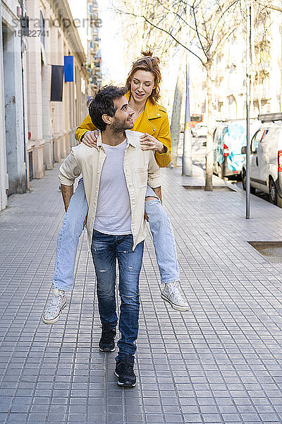 Mann nimmt seine Freundin huckepack auf dem Bürgersteig in der Stadt