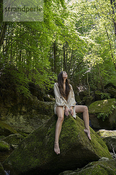Junge Frau sitzt auf einem Felsen im Wald  Garrotxa  Spanien