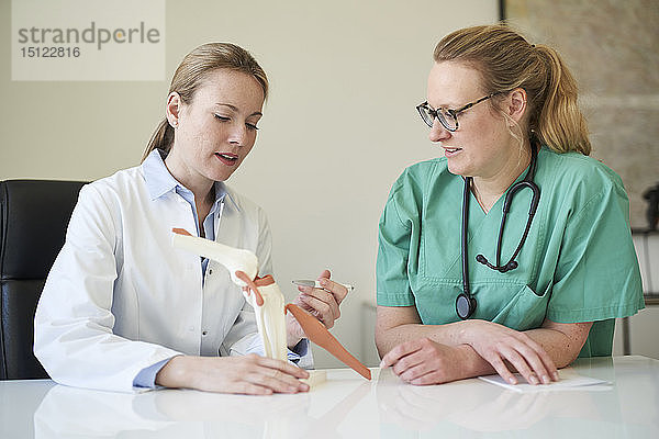 Ärztin und Frau in OP-Kleidung mit Kniegelenkmodell im Gespräch