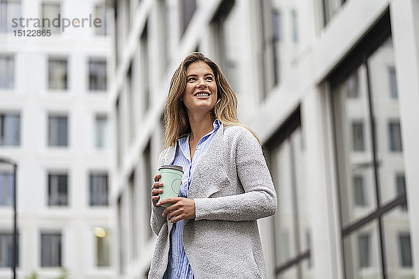Junge Geschäftsfrau mit Kaffee zum Mitnehmen  im Hintergrund das Bürogebäude