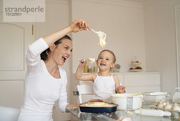Glückliche Mutter und kleine Tochter backen zu Hause in der Küche gemeinsam einen Kuchen