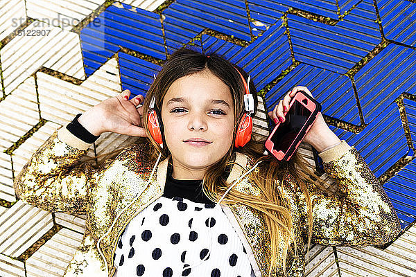 Porträt eines Mädchens in goldener Paillettenjacke  das mit Kopfhörer und Smartphone Musik hört