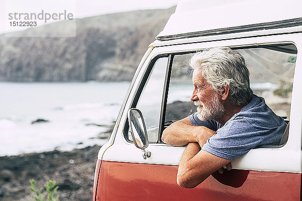 Älterer Mann reist in einem Kleinbus und schaut auf das Meer