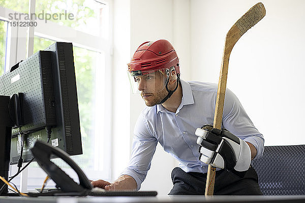 Als Eishockeyspieler verkleideter Geschäftsmann arbeitet am Schreibtisch im Büro