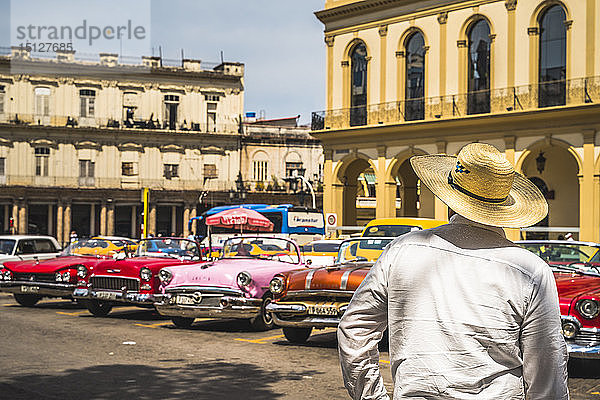 Kubanischer Mann mit Blick auf bunte alte amerikanische Taxis  die in Havanna  La Habana  Kuba  Westindien  Karibik  Mittelamerika geparkt sind
