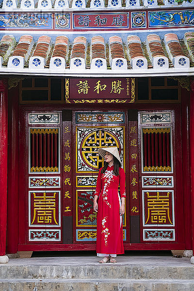 Eine junge Vietnamesin trägt ein traditionelles Ao-Dai-Kleid und steht vor einem Tempel im historischen Stadtzentrum  Hoi An  Vietnam  Indochina  Südostasien  Asien