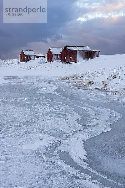 Fischerhäuser und Eisformationen mit dramatischem Himmel im Winter  Eggum  Lofoten-Inseln  Arktis  Norwegen  Europa