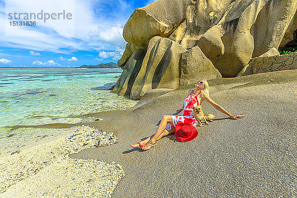 Touristin und süßer Hund bei Ebbe am Strand sitzend  mit Granitfelsen dahinter  an der Anse Source d'Argent  La Digue  Seychellen  Indischer Ozean  Afrika
