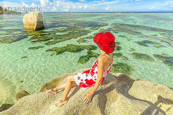 Touristin mit rotem Hut auf einem Granitfelsen an der Anse Source d'Argent  Insel La Digue  Seychellen  Indischer Ozean  Afrika