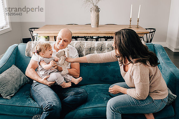 Mutter und Vater auf dem Sofa  während die kleine Tochter mit einem Plüschtier spielt