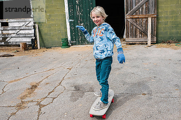 Blonder Junge fährt Skateboard auf dem Bauernhof