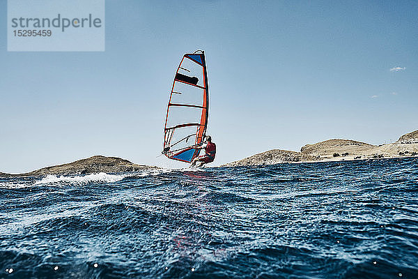 Zurückgelehnter junger Mann beim Windsurfen auf Meereswellen  Seitenansicht  Limnos  Khios  Griechenland