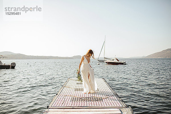 Junge Braut im Brautkleid beim Spaziergang am windigen Seepier  Stresa  Piemont  Italien