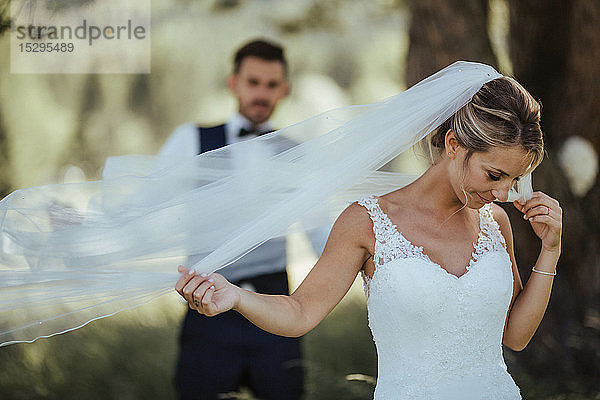 Braut und Bräutigam halten zarten Hochzeitsschleier im Wald