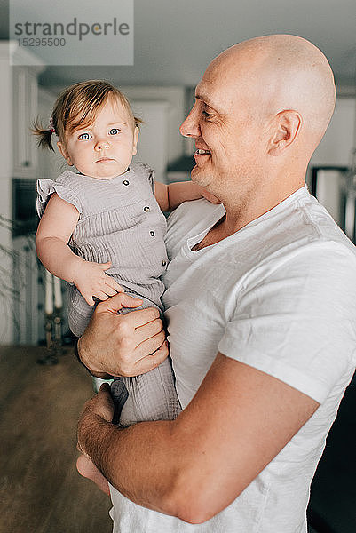 Vater trägt Baby-Tochter im Wohnzimmer  Porträt